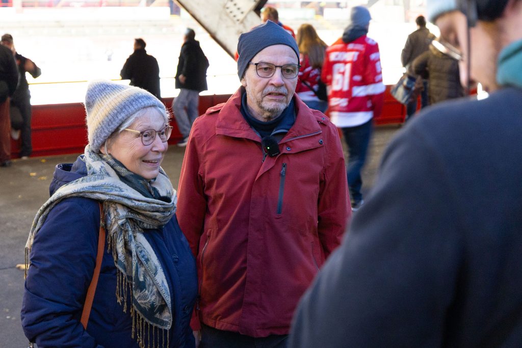Volksbank‑Mitglieder stehen im Stadion des EC Bad Nauheim und erzählen begeistert von ihrem Eishockey‑Erlebnis.