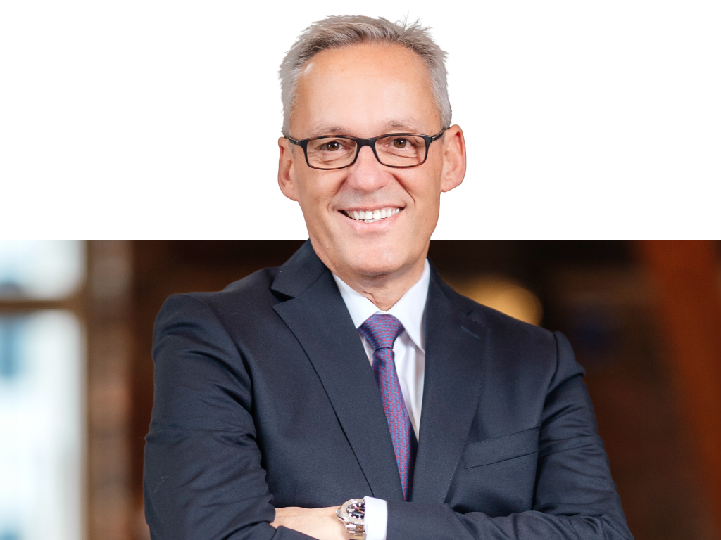 Ein Vorstandssprecher der Volksbank Mittelhessen steht im Business‑Anzug vor einem modernen Hintergrund.