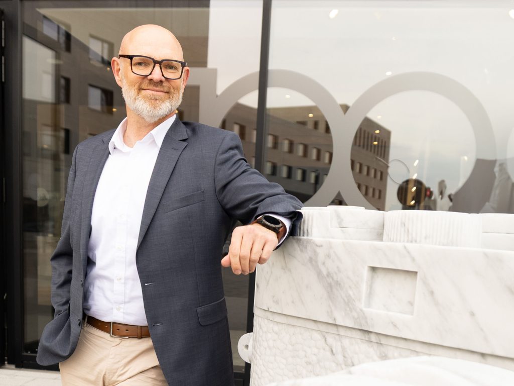 Malte Klingelhöfer lehnt an einer großen Marmorskulptur in Form einer Kamera auf dem Gelände des Leitz‑Parks in Wetzlar.