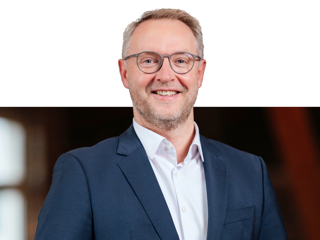 Ein Vorstandsmitglied der Volksbank Mittelhessen steht im Business‑Anzug vor einem modernen Hintergrund.
