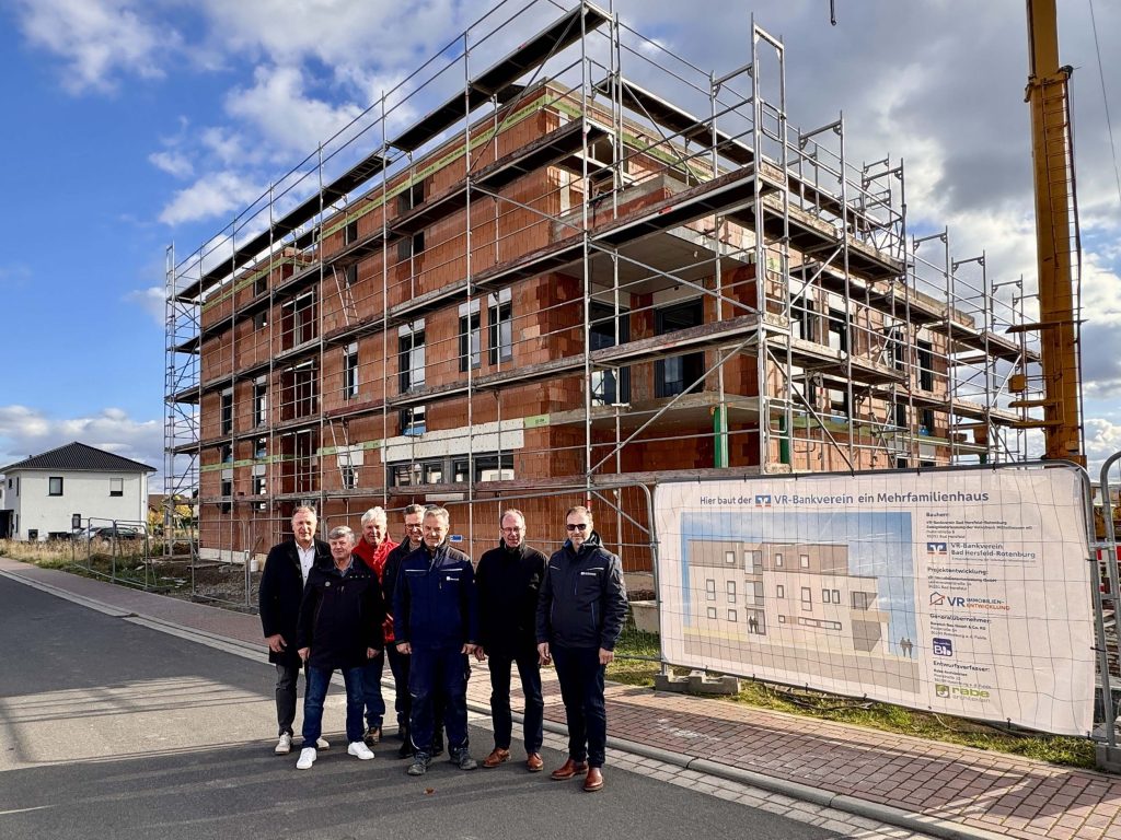 Baustelle eines Mehrfamilienhaus des VR‑Mitgliederwohnens, eingerüstet und von mehreren Projektbeteiligten vor Ort begutachtet.