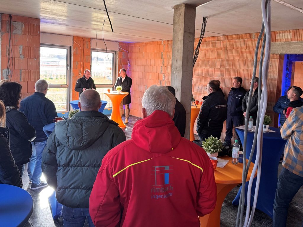 Vertreter von VR-Bankverein Bad Hersfeld-Rotenburg und der beteiligten Handwerksfirmen stehen im Inneren des Rohbaus eines neuen Mehrfamilienhauses in Obersuhl.